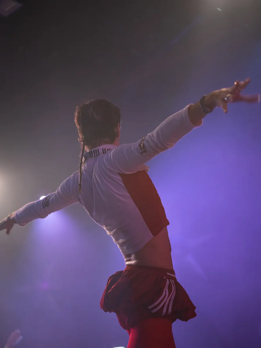 A performer with both arms out wide on stage in purple light